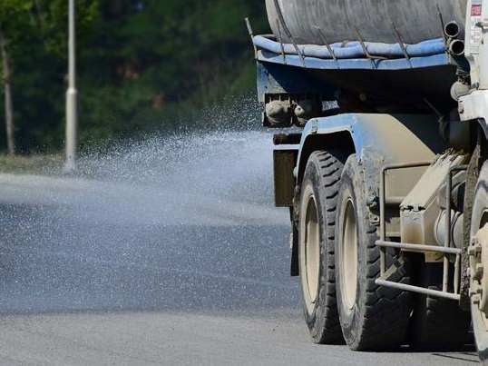 Truck spraying dust suppressant on road.       